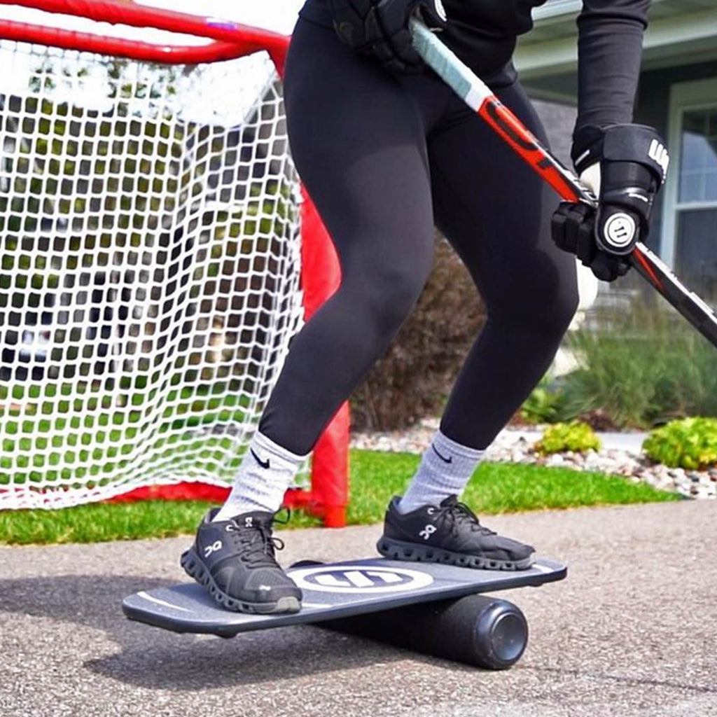 a player balancing on the balance board with a hockey stick in a driveway